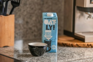 Bitkisel Sütler Rehberi: Oatly Yulaf Sütü ve Hindistan Cevizi Sütü 1 Mermer tezgahta Oatly yulaf sütü kartonu ve espresso fincanı