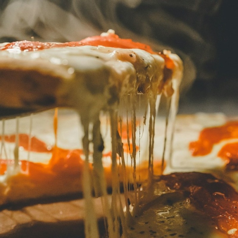 Fırından yeni çıkmış pizza diliminde erimiş mozzarellanın uzaması